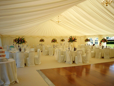Wedding reception place settings under large tent and floral center pieces.